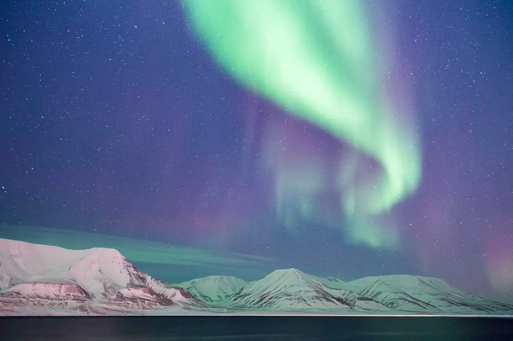 View of the Northern Lights in the sky above white mountains in Svalbard