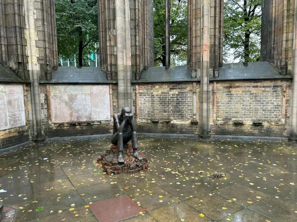 statue of a person holding their head sitting on bricks in the Church of St Nicholas