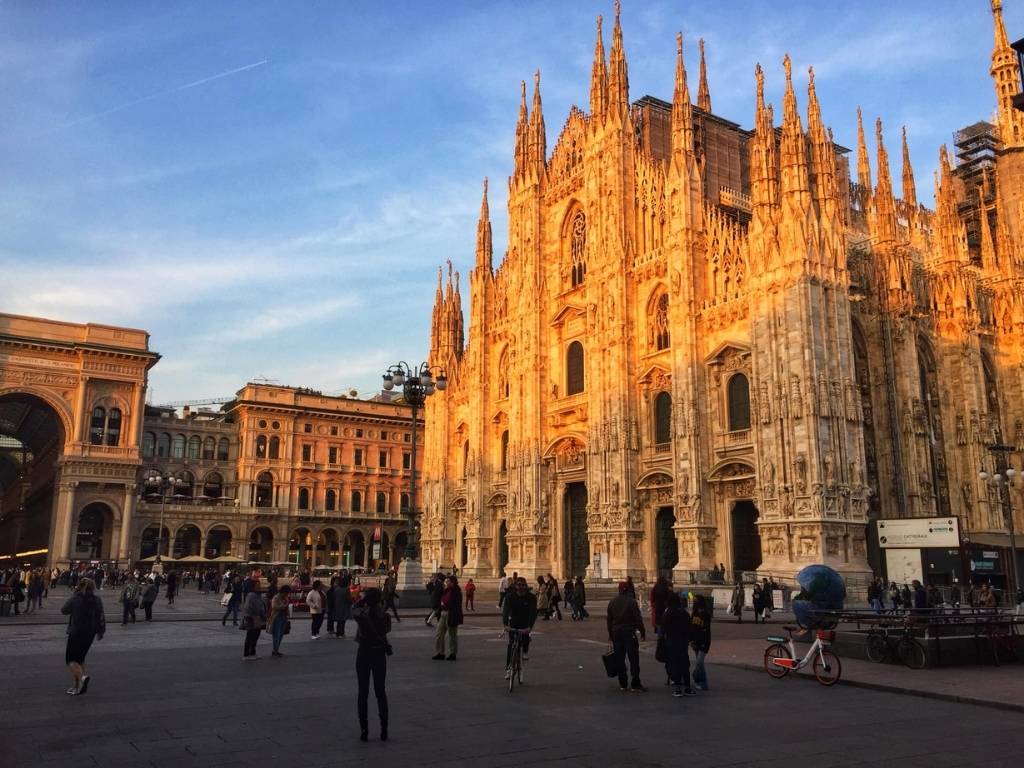 The Duomo cathedral in Milan, towering white building with a piazza in front of it