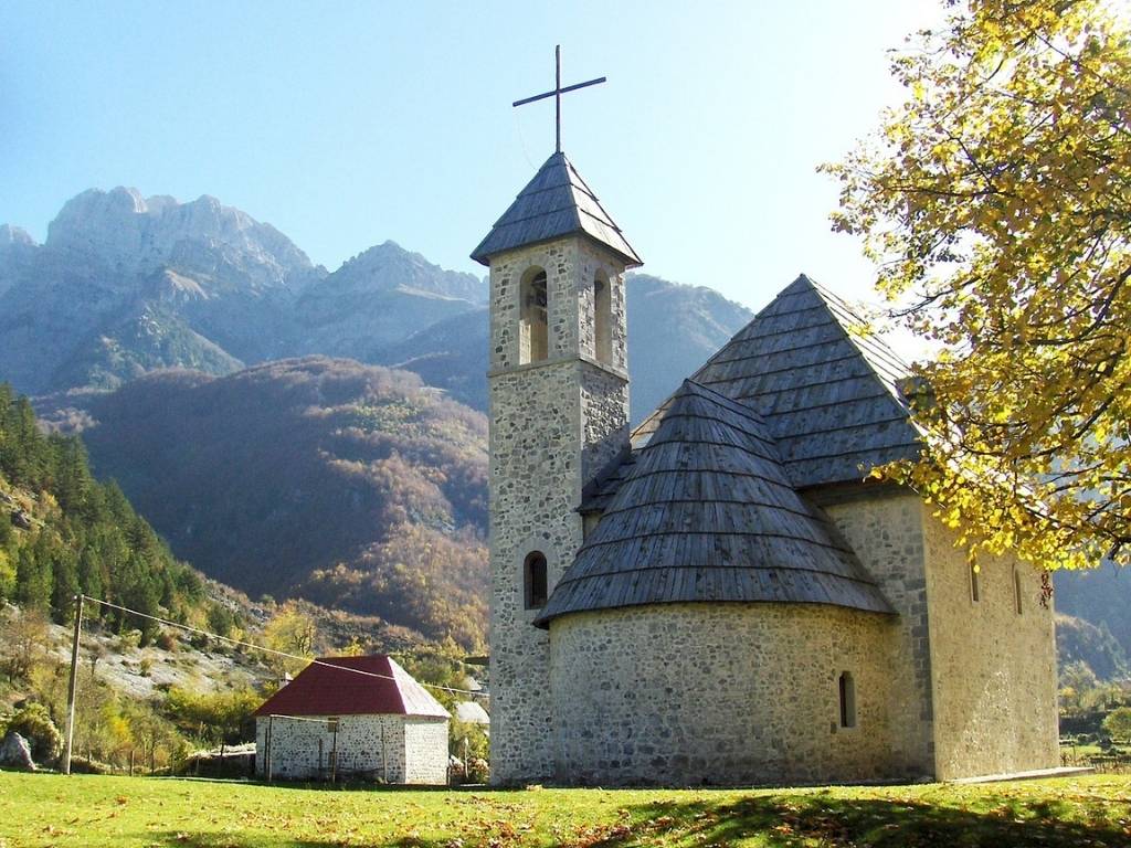 Stone castle in Theth Albania, with a big cross atopt the roof against the backdrop of mountains