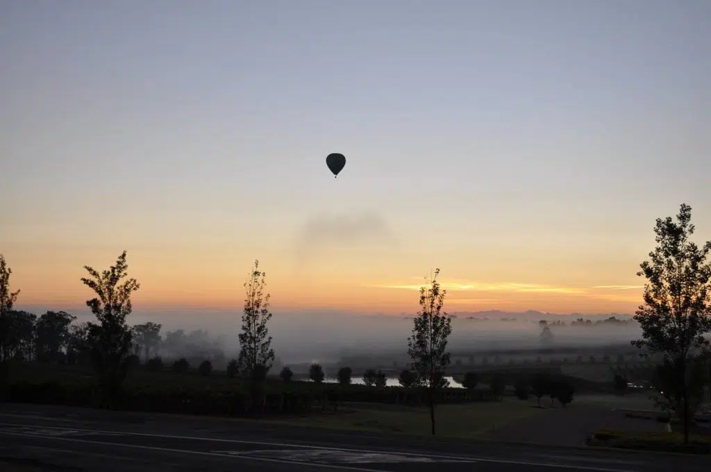hot air balloon rising into the sky during a sunrise at hunter valley