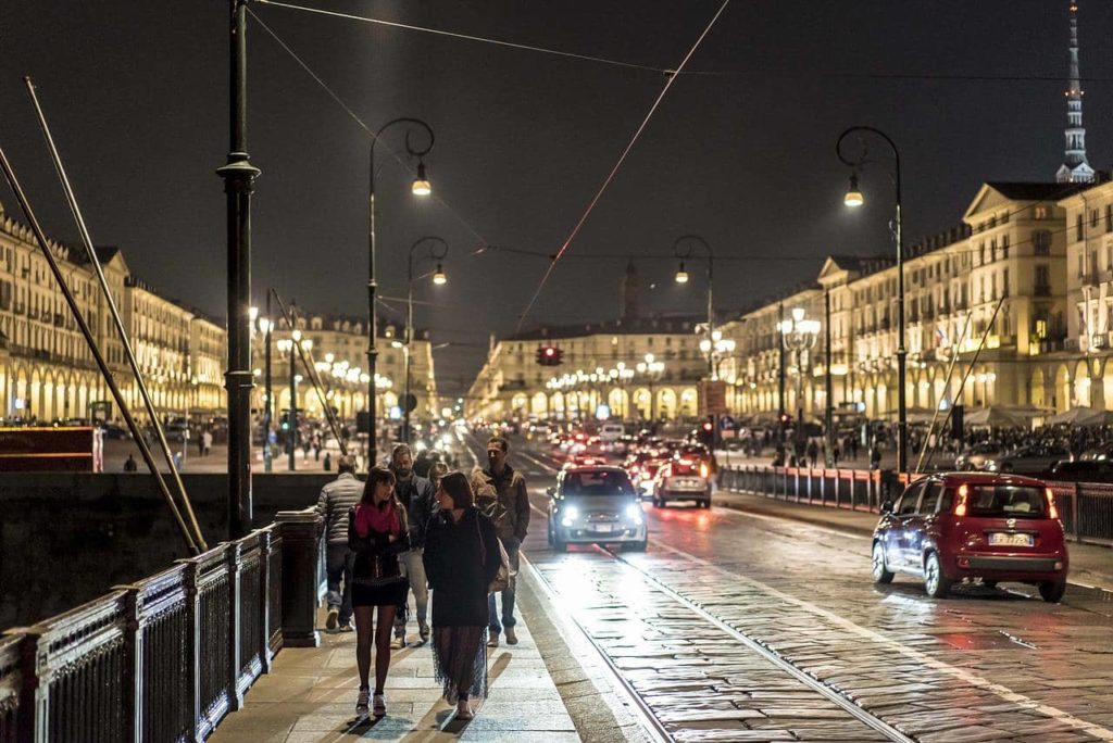 street in turin at night with people walking on the pavement and cars driving past