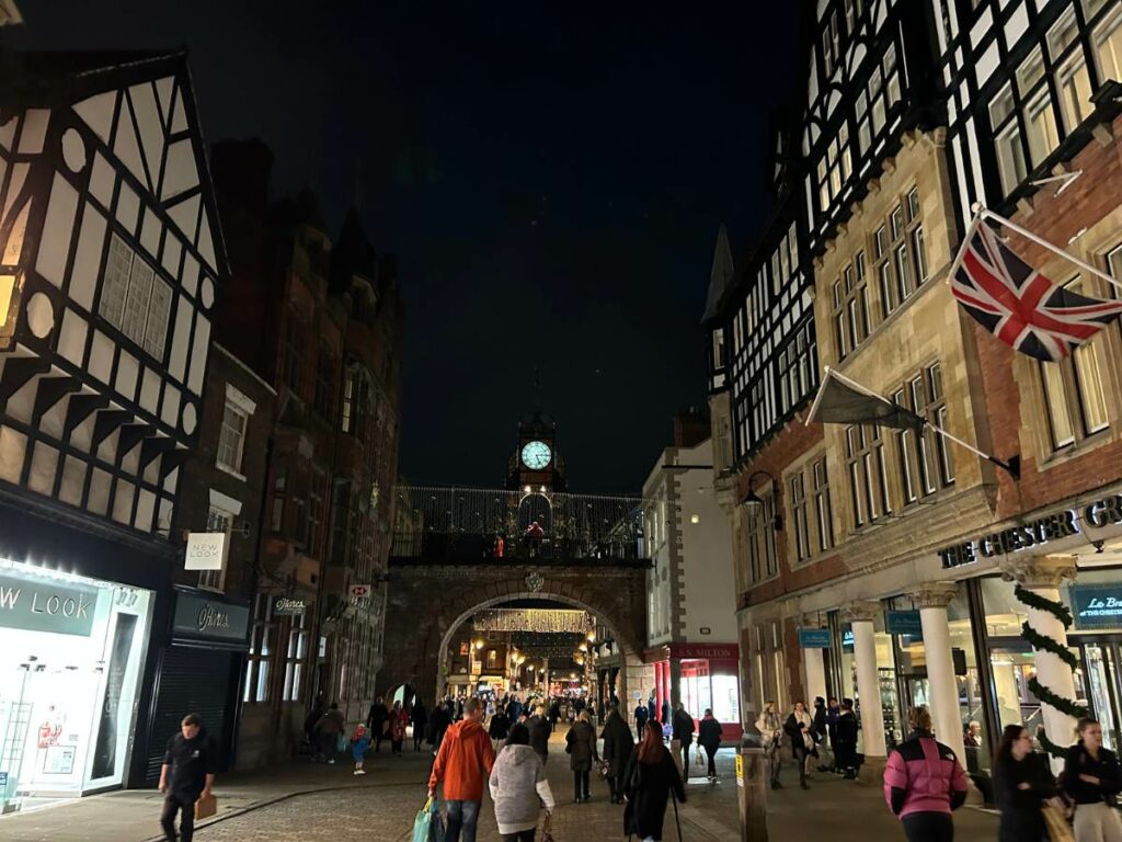 walking down Foregate Street in Chester at night with the Eastgate Clock visible in the background