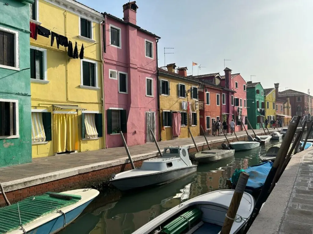 walking along the canal in Burano with multi-colored houses in the background