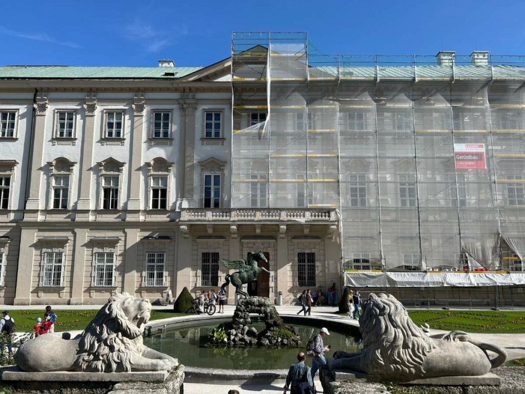 exterior of mirabell palace with scaffolding covering part of it and the pegasus fountain in front
