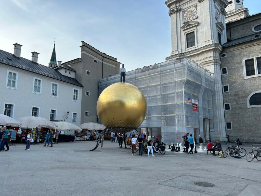 a sculpture of a gold sphere with a figure on top of it in a square in salzburg